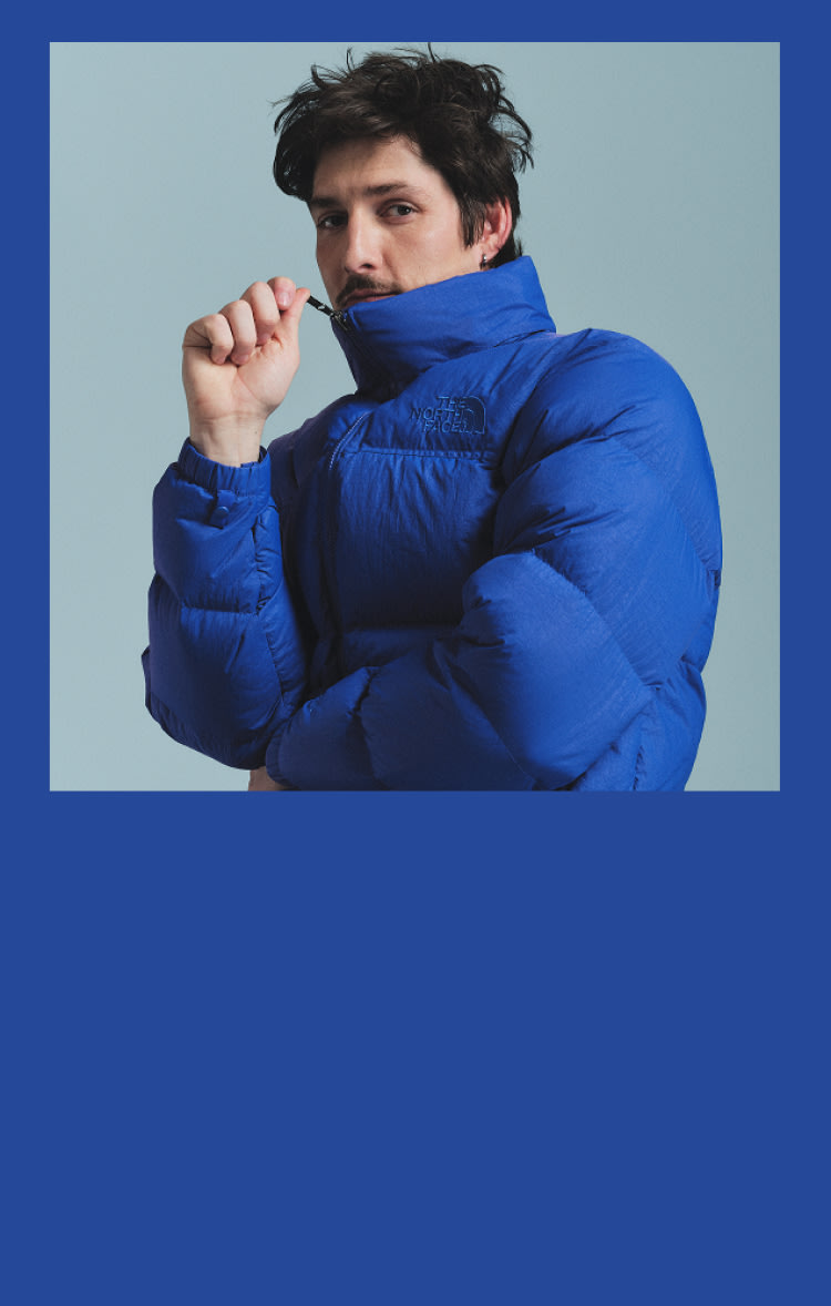 A man in a blue Nuptse all the way zipped, the image has a blue frame around it.