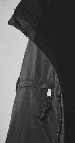 Une version noire de la veste 1995 Casentino Denali est suspendue à un cintre en métal sur un fond clair.