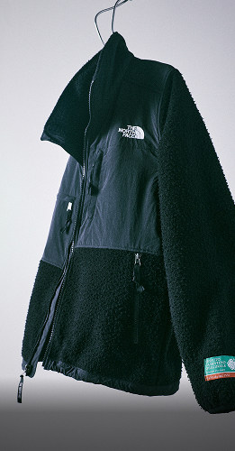 Une version noire de la veste 1995 Casentino Denali est suspendue à un cintre en métal sur un fond clair.