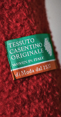 Une photo détaillée d’une étiquette tissée verte portant la mention « Tessuto Casentino Originale Woven in Italy », cousue sur le molleton texturé rouge.
