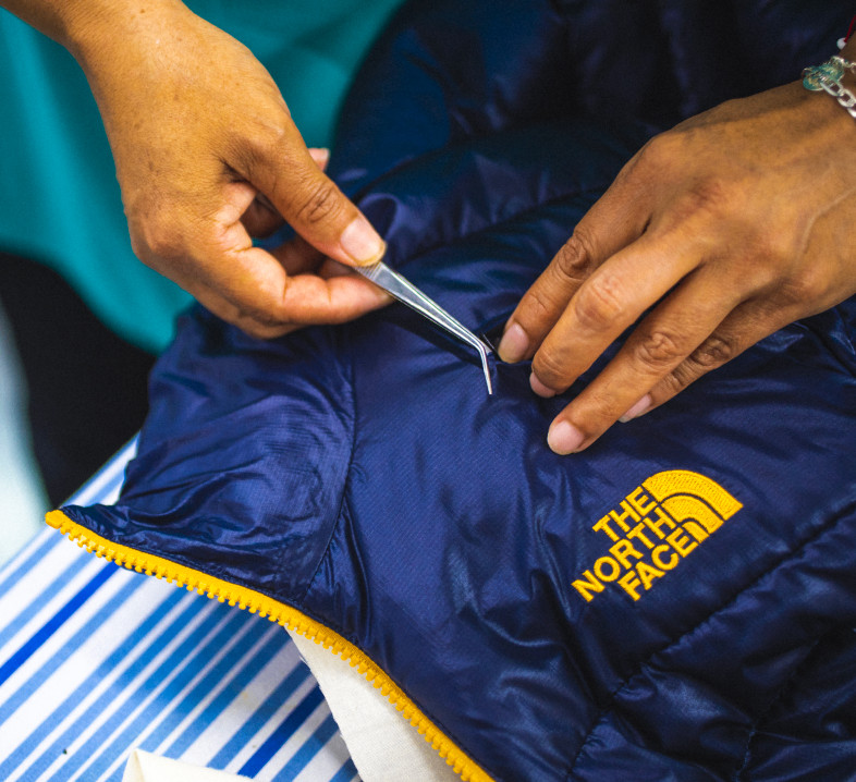 A person repairing a jacket from The North Face