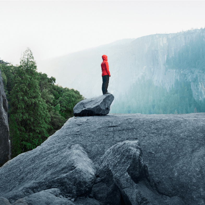 A hiker stands on a rock in front of a mountain.