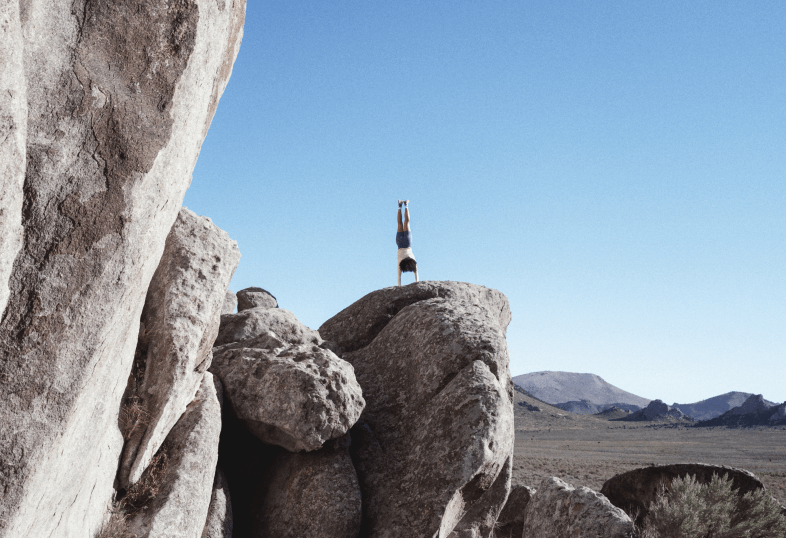 Un mannequin faisant un équilibre sur les mains sur un gros rocher, vêtu de la collection activewear Jaida.