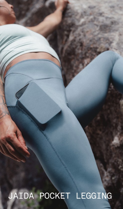 Close-up of a model wearing the A model wearing the Jaida Tank in Opal Frost and the Jaida Pocket Leggings in Granite Grey, shown against a rocky surface.
