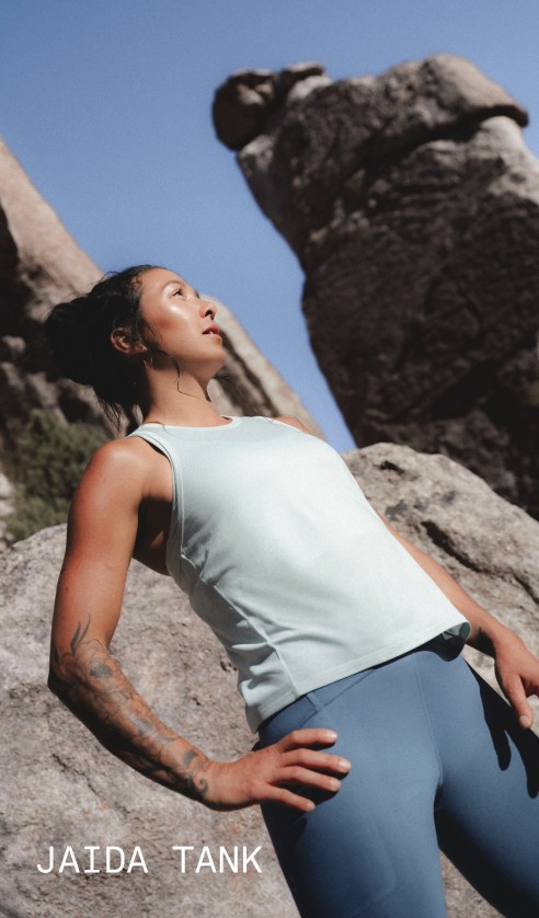 A model wearing the Jaida Tank in Opal Frost and the Jaida Pocket Leggings in Granite Grey stands among outdoor rock formations.