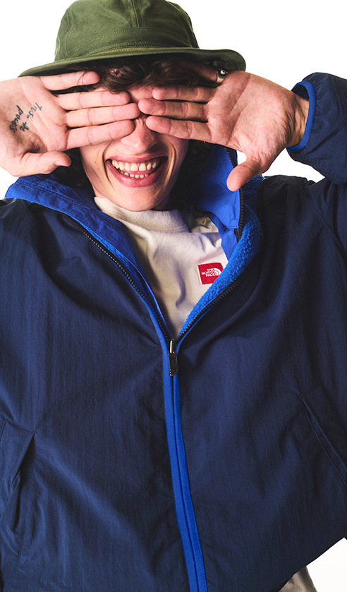 A guy in a blue jacket and a green hat covering his eyes