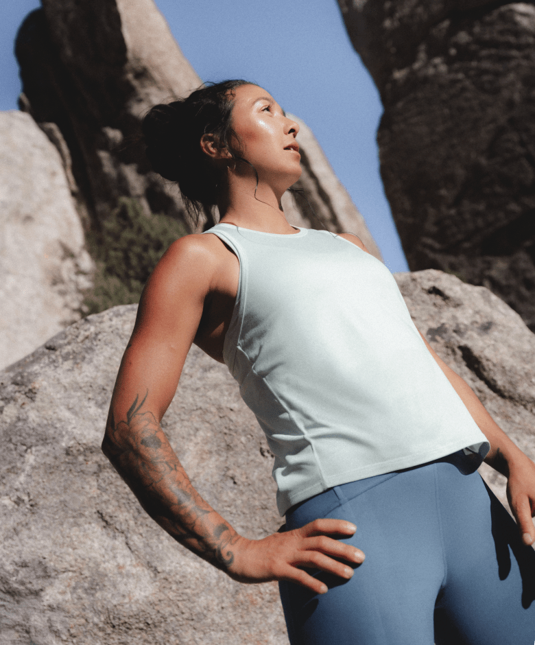 Athlete wearing the Jaida Tank in Opal Frost and the Jaida Pocket Leggings in Granite Grey stands among outdoor rock formations.