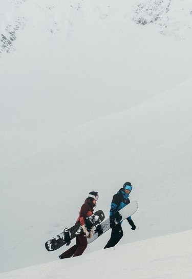 Two snowboarders hike across a snowy slope. 