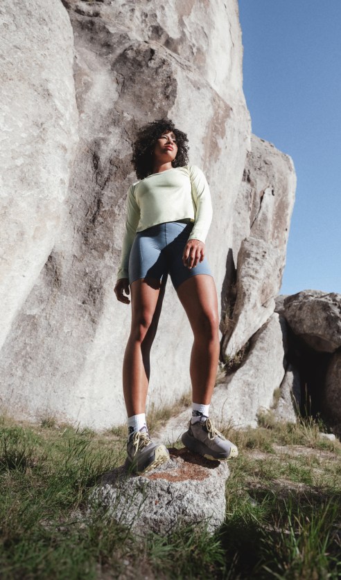 Athlete wearing the Jaida Long Sleeve in White Dune stands among large rock formations in an outdoor setting.
