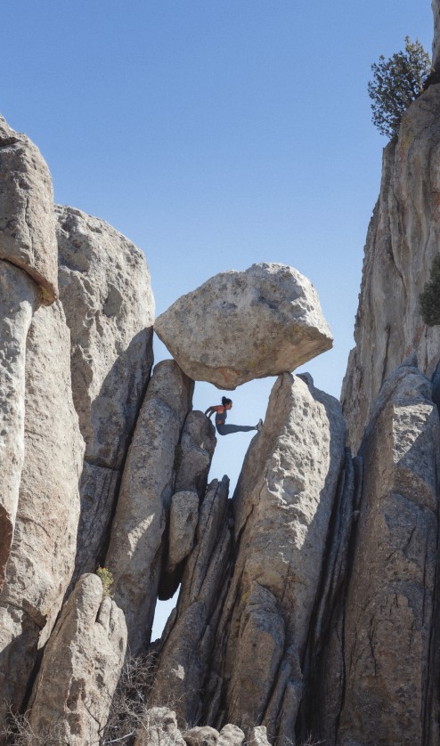 Athlete wearing the Jaida Long Sleeve in White Dune stands among large rock formations in an outdoor setting.
