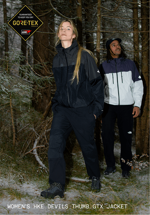 Woman in black jacket standing in forest.