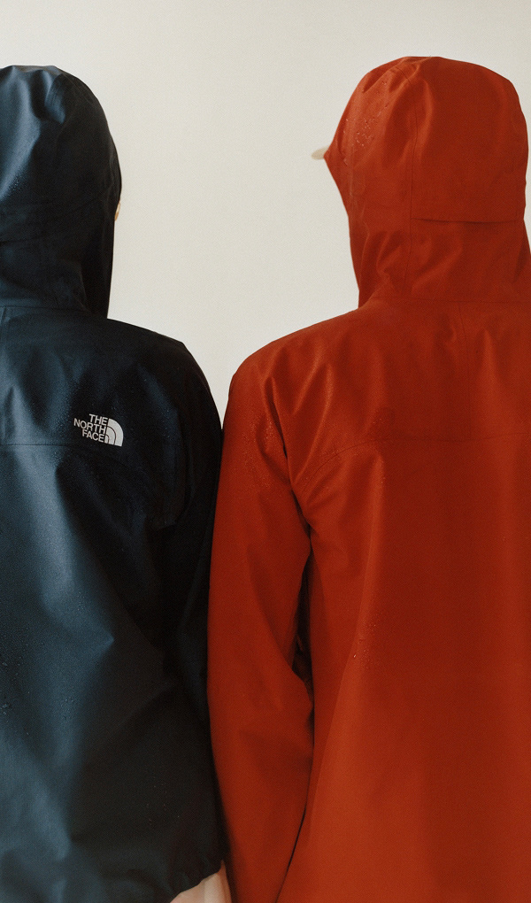 The backs of two individual wearing red and navy rain jackets.