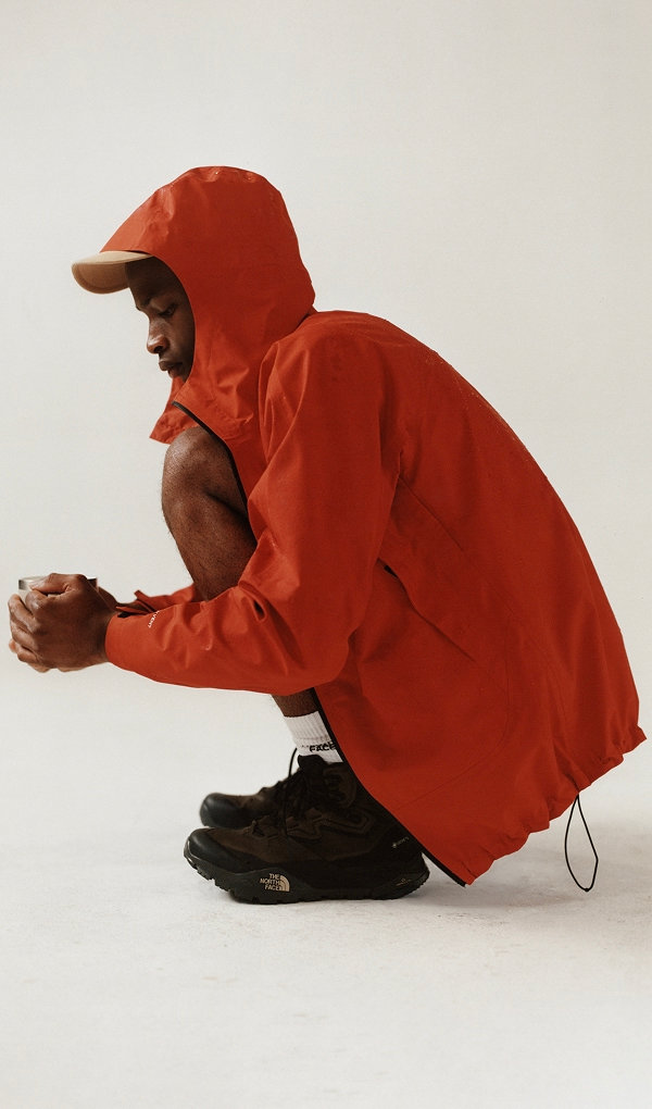 Man squatting down wearing a red rain jacket. 