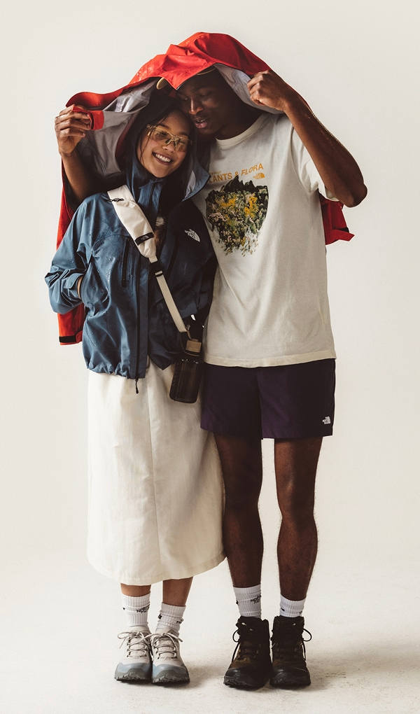 Man holding up a red rain jacket over him and a girl. 