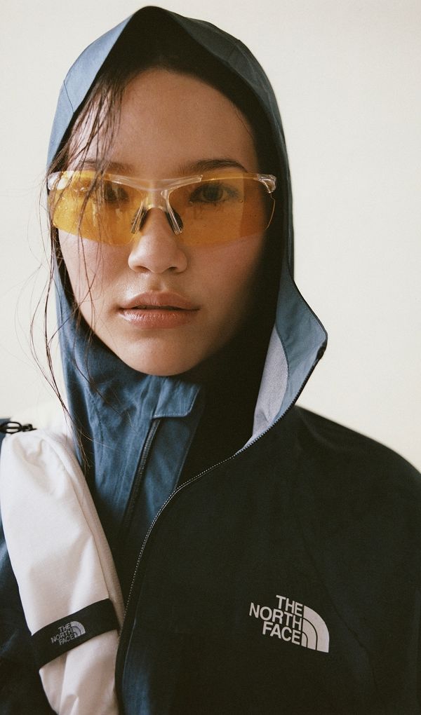 Close up of woman wearing blue rain jacket and yellow sunglasses. 