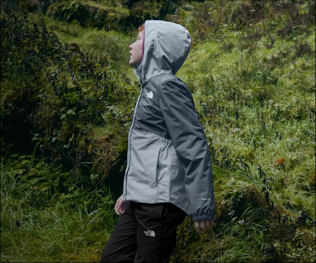 Kid wears grey rain jacket near moss.