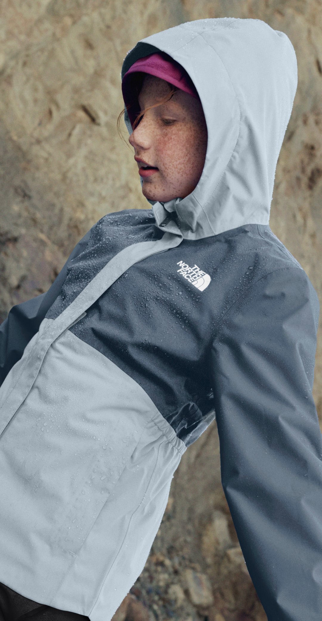 Kid wears grey rain jacket near boulder. 