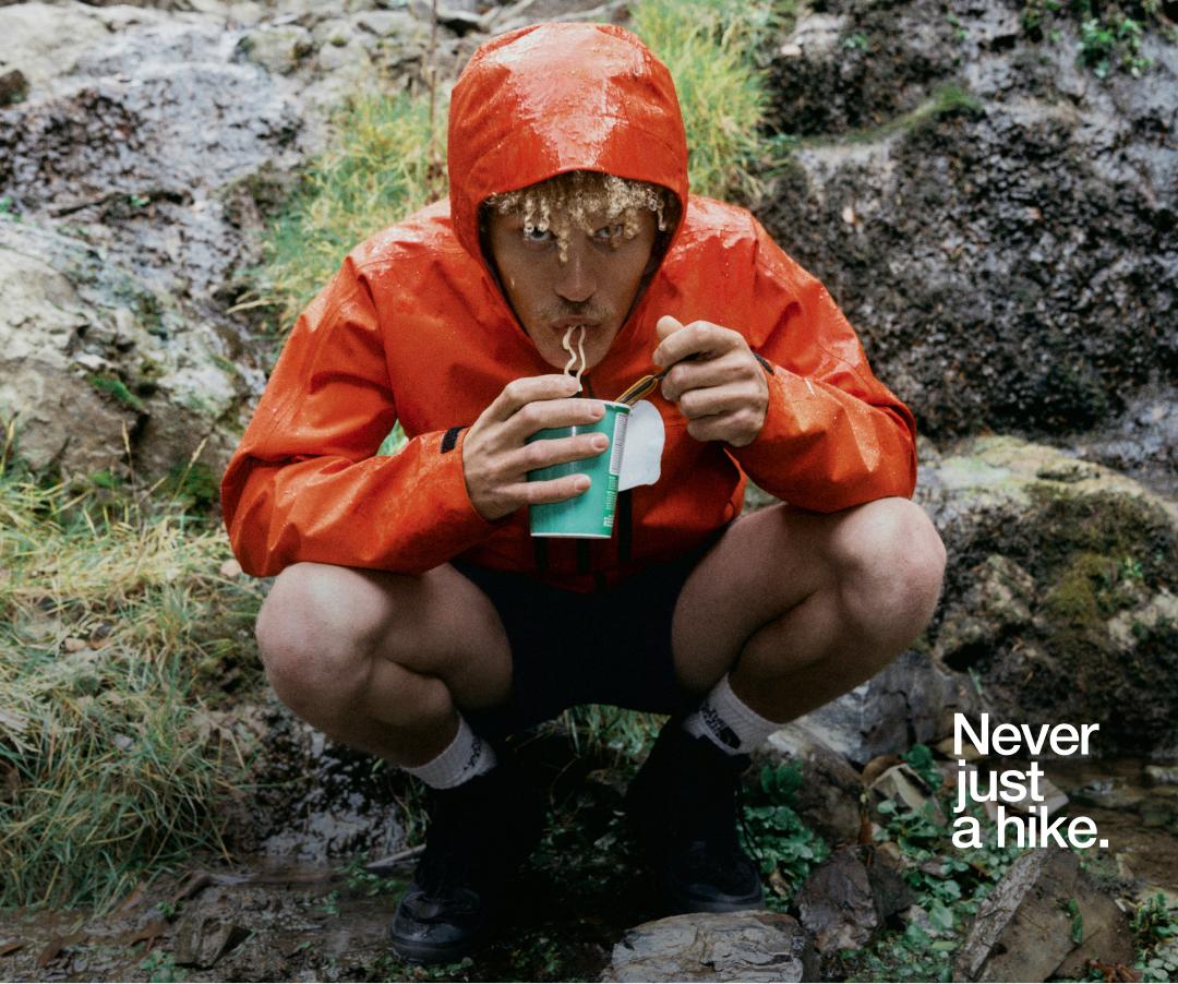 Man eating noodles next to boulder in rain jacket