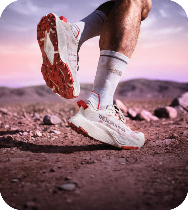 Two legs wearing white Altamesa 500 V2 shoes and The North Face crew socks going for a jog in high-mountain terrain.