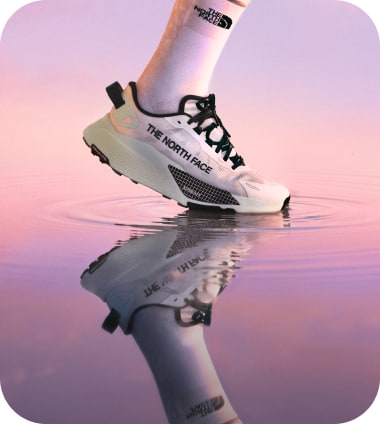 Two legs wearing white Altamesa 500 V2 shoes and The North Face crew socks going for a jog in high-mountain terrain.