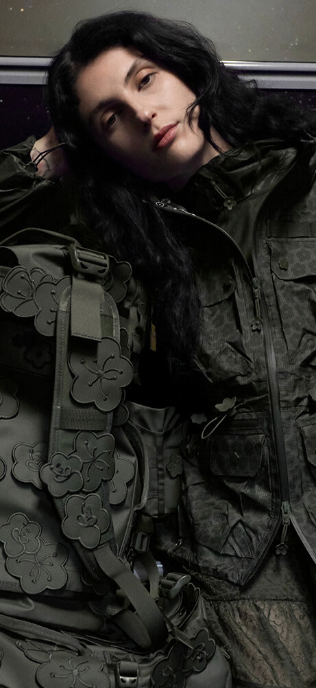 A model sitting on a train wearing The North Face x Cecilie Bahnsen collection with a Anna Base Camp Duffel bag.