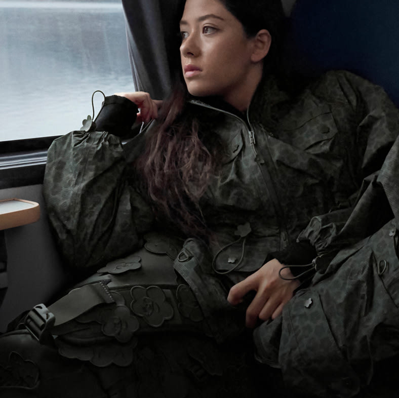 Model in The North Face x Cecilie Bahnsen collection relaxing on a train seat with alpine mountains visible through the window.