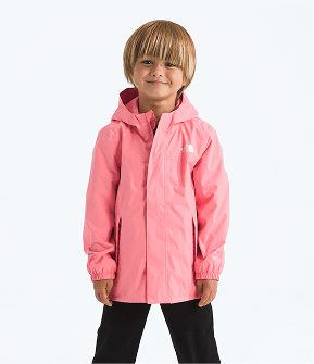 Toddler wearing a pink jacket and black pants, arms at sides, smiling slightly and facing the camera. 