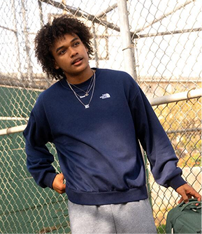 A young man wearing a navy sweatshirt with chain-link fences in the background. 