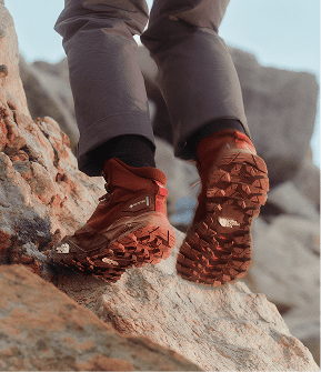 Closeup of the back of orange hiking shoes. Person walking up rocky terrain. 