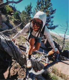 Woman wearing sunglasses and a white hoodie hiking up a mountain slope. 