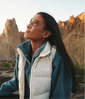 Woman wearing blue fleece jacket and white vest facing left, looking up. 