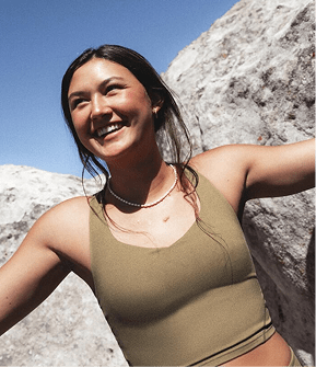 Woman in brown tank top, smiling, looking at something off screen.
