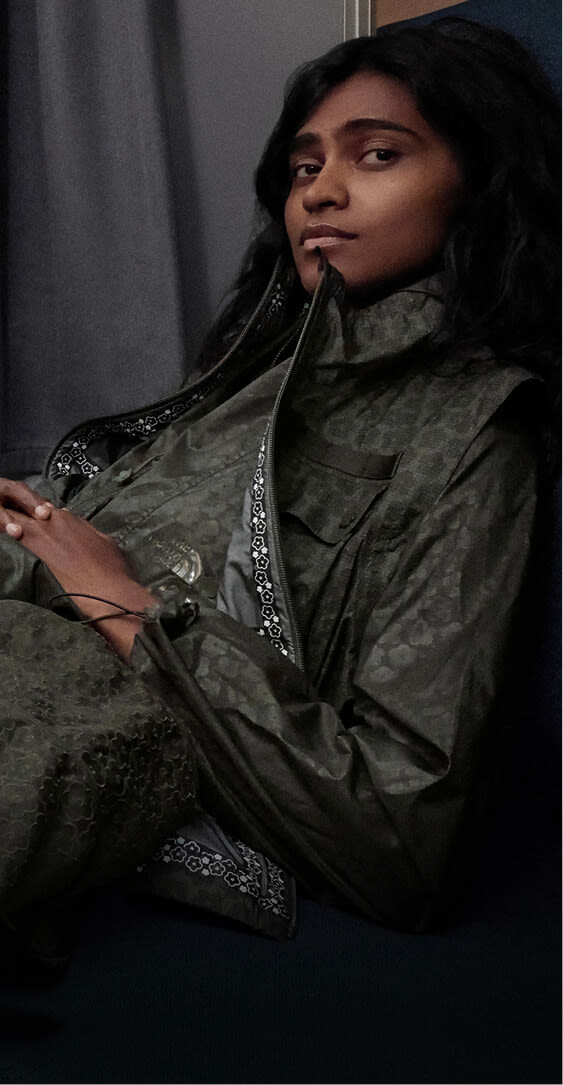 Model in The North Face x Cecilie Bahnsen collection relaxing on a train seat with alpine mountains visible through the window.