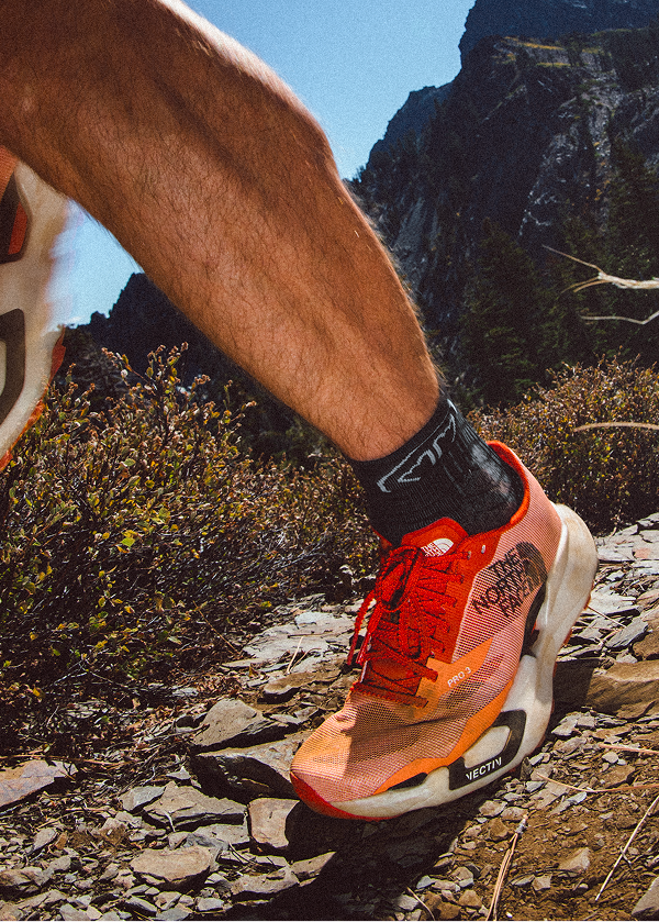 Close up of a red north face Vectiv shoe running up a trail.