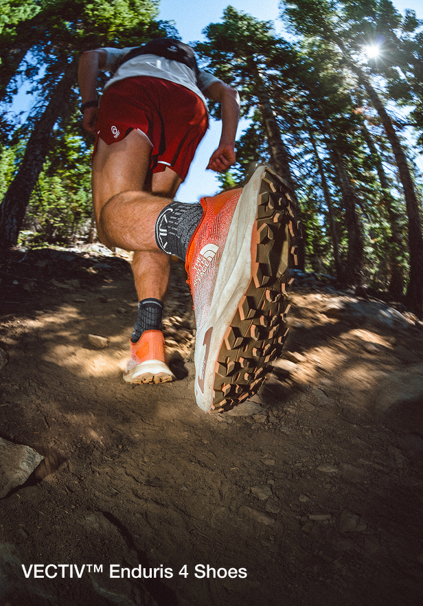 close up of back of the enduris 4 shoes while a man is running on a trail in a forest.
