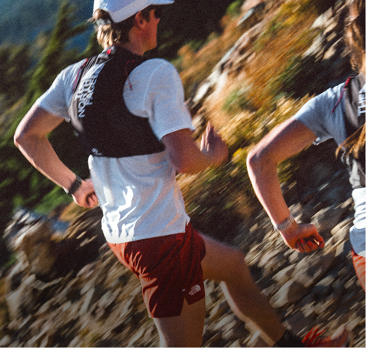 Back of person running wearing a white shirt, black vest and red Pacesetter Shorts. 