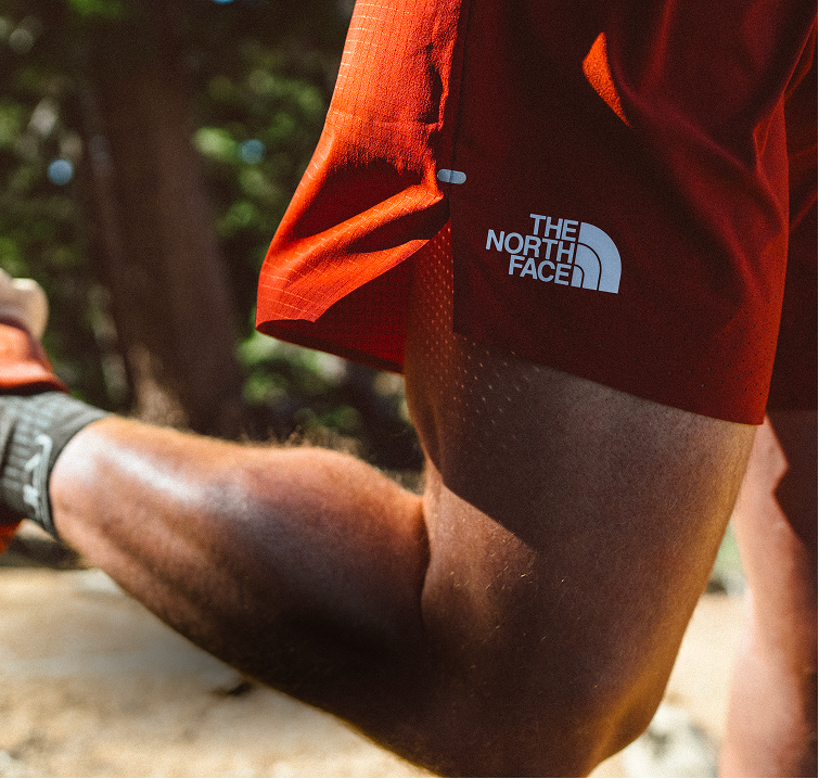 Closeup of red Pacesetter Shorts on runner. Leg is kicked back in mid-stride, The North Face logo is clearly visible.