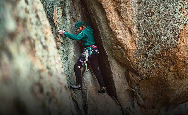 Female climber climbing out of a crevice in a boulder wall.