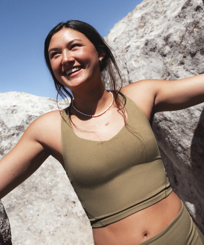Athlete wearing the Jaida Long Line Bra and Jaida Pocket Leggings in Cedar stands among rock formations outdoors. 