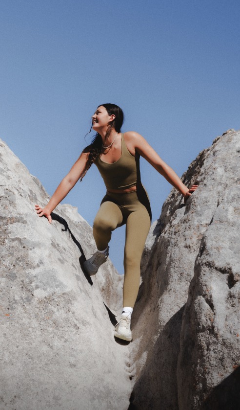 Athlete climbing between large rock formations wearing Jaida Pocket Leggings in an outdoor desert landscape.