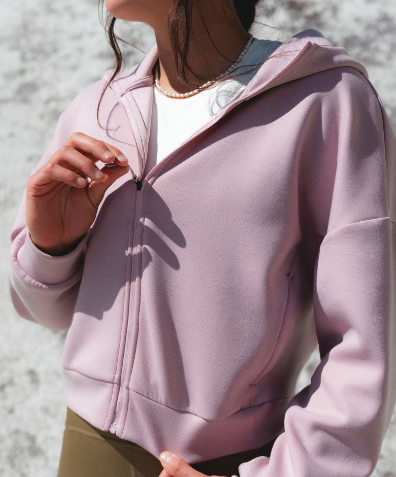 Close-up of an athlete wearing the Jaida Full Zip Hooded Jacket in Metal Pink layered over activewear in an outdoor setting.