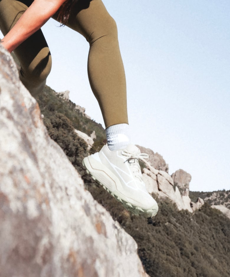 Close-up of an athlete stepping across rocky terrain wearing the Fastpack Shoes in Desert Stone and Lemon Mist. 