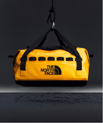 Yellow Base Camp Waterproof Duffel hanging from a hook, highlighting its rugged waterproof construction.