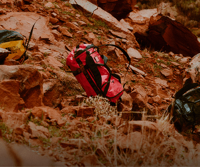 Three North Face Duffle Bags placed along a rocky hill.