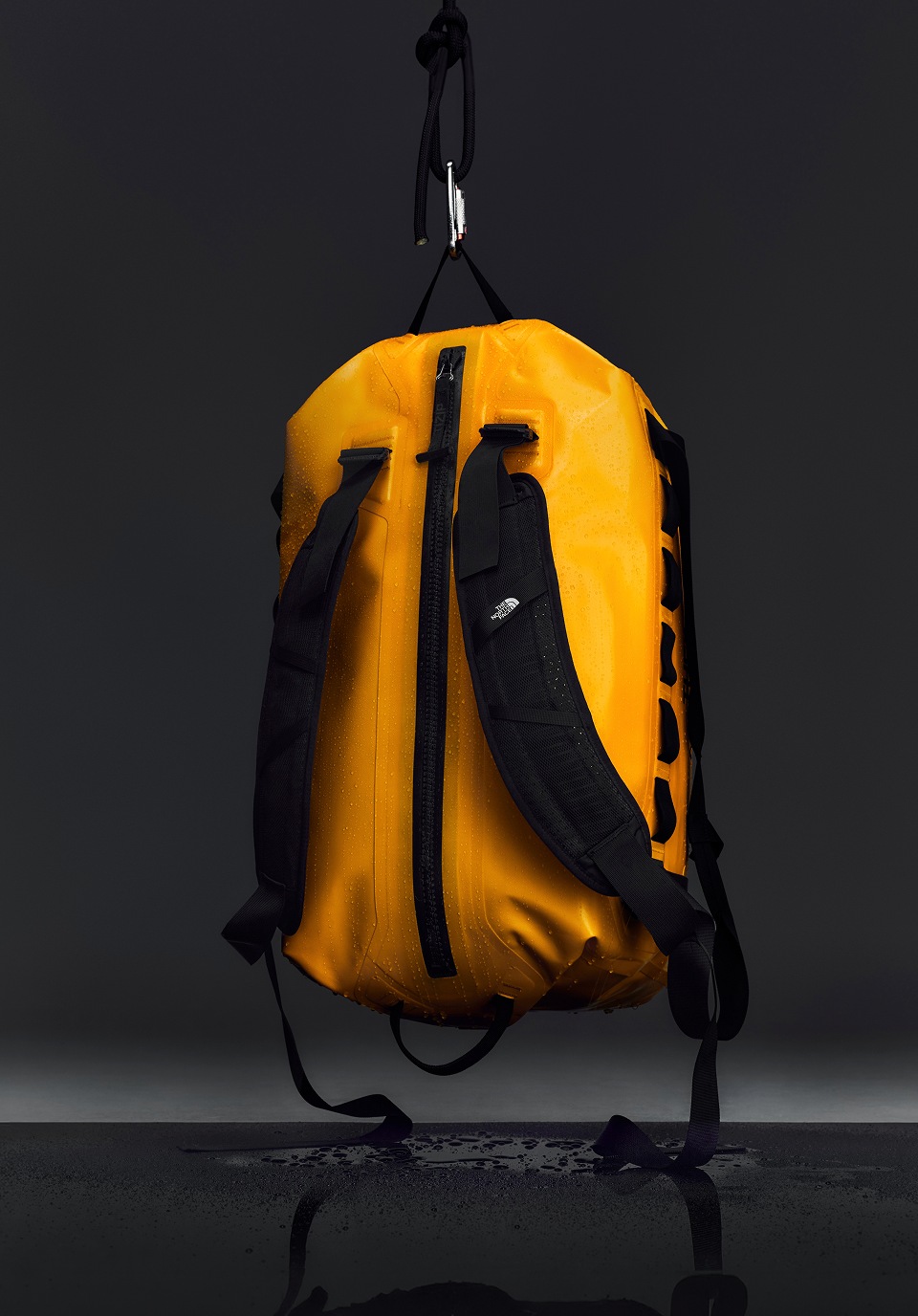 Yellow base camp duffel bag hanging from the ceiling in a studio with black bankground.  