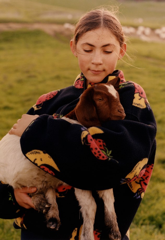 A woman holds a goat wearing a fleece from The North Face x Sky High Farm Goods collaboration. 