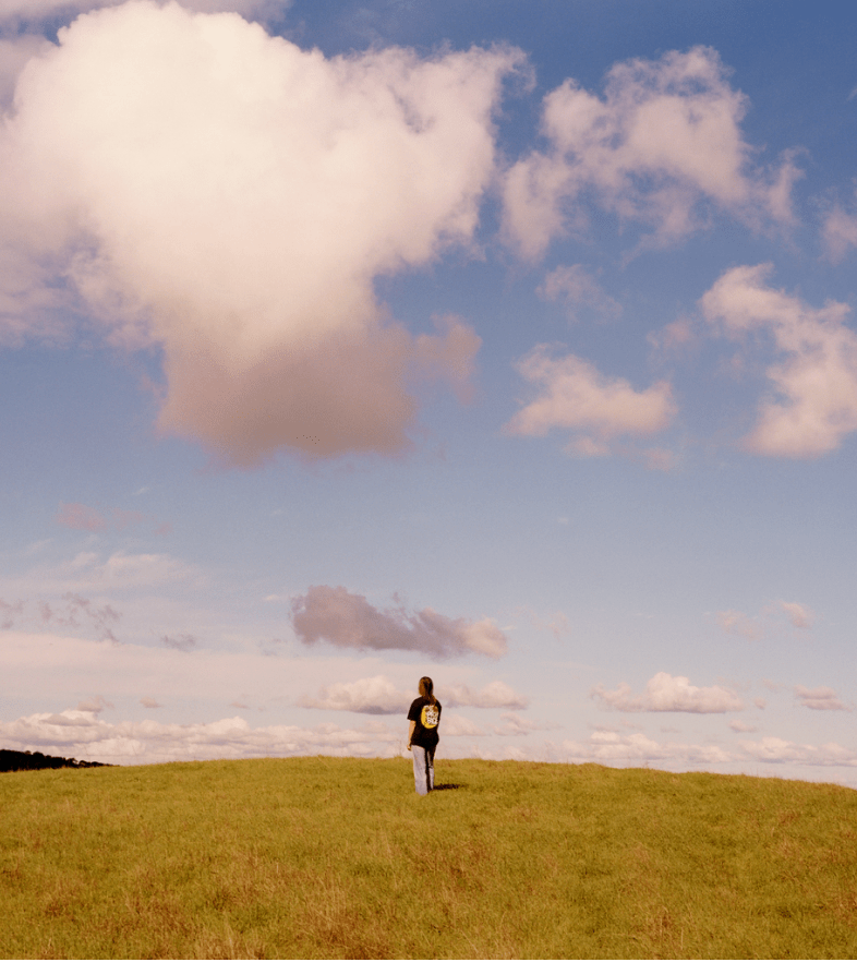 A woman stands on a grassy hill in her The North Face x Sky High Farm Goods tee.  
