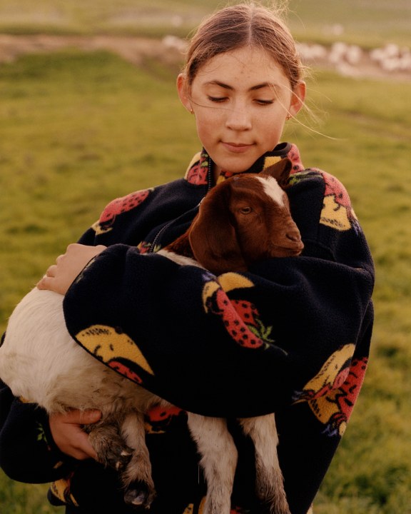 A woman holds a goat wearing a fleece from The North Face x Sky High Farm Goods collaboration. 