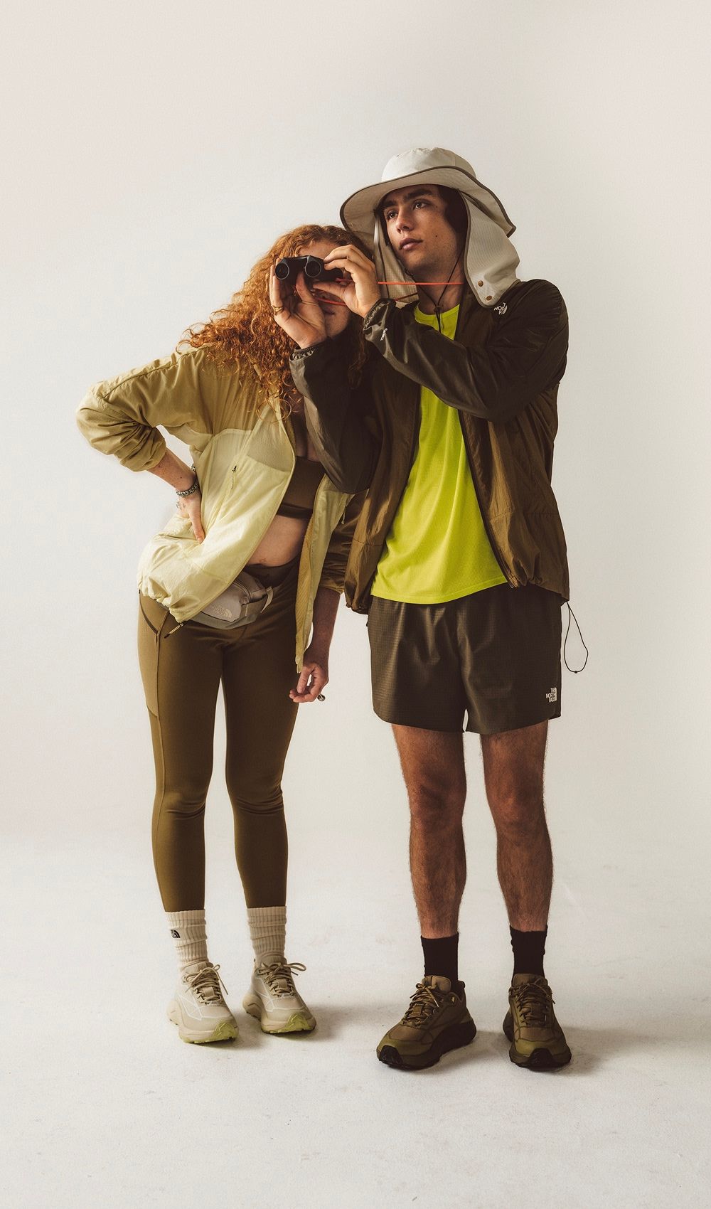 Un homme portant un chandail jaune et une veste brune debout avec une femme portant une veste jaune, sur fond blanc.