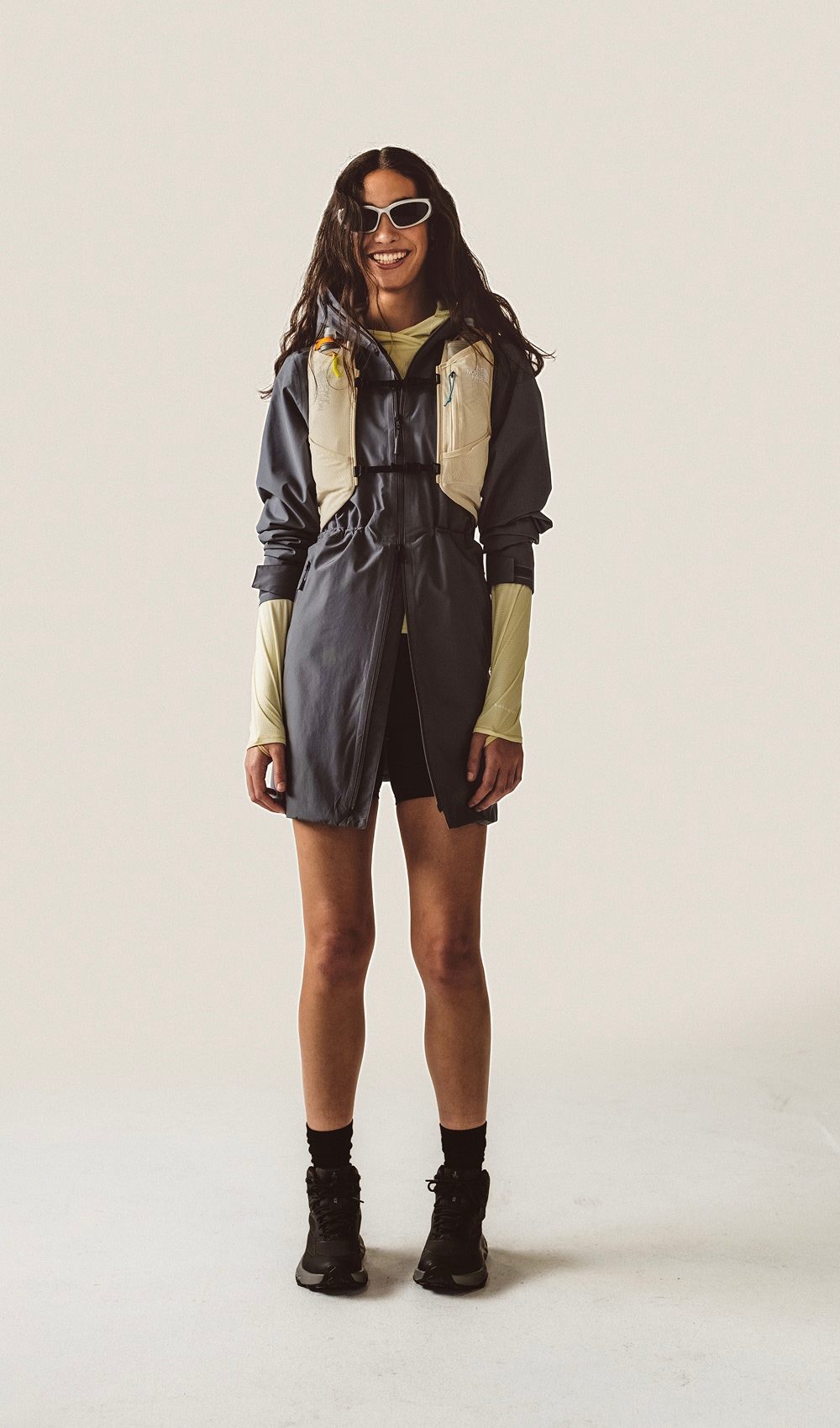 Une femme debout, portant une veste bleue et un gilet de course blanc, sur fond blanc.